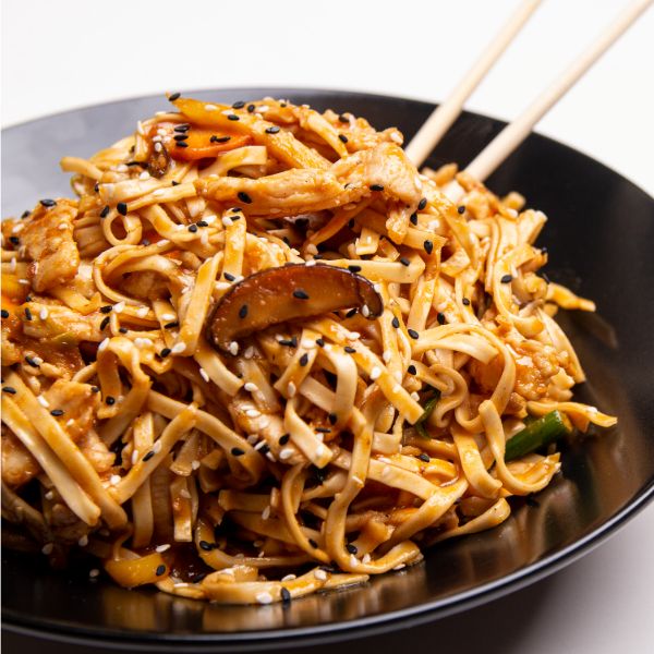 Asian noodles με κοτόπουλο, λαχανικά, μανιτάρια και σουσάμι σε μαύρο πιάτο.