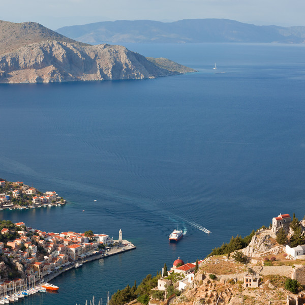 Θέα σε ελληνικό νησί με γαλάζια θάλασσα, παραδοσιακά σπίτια και λιμάνι.